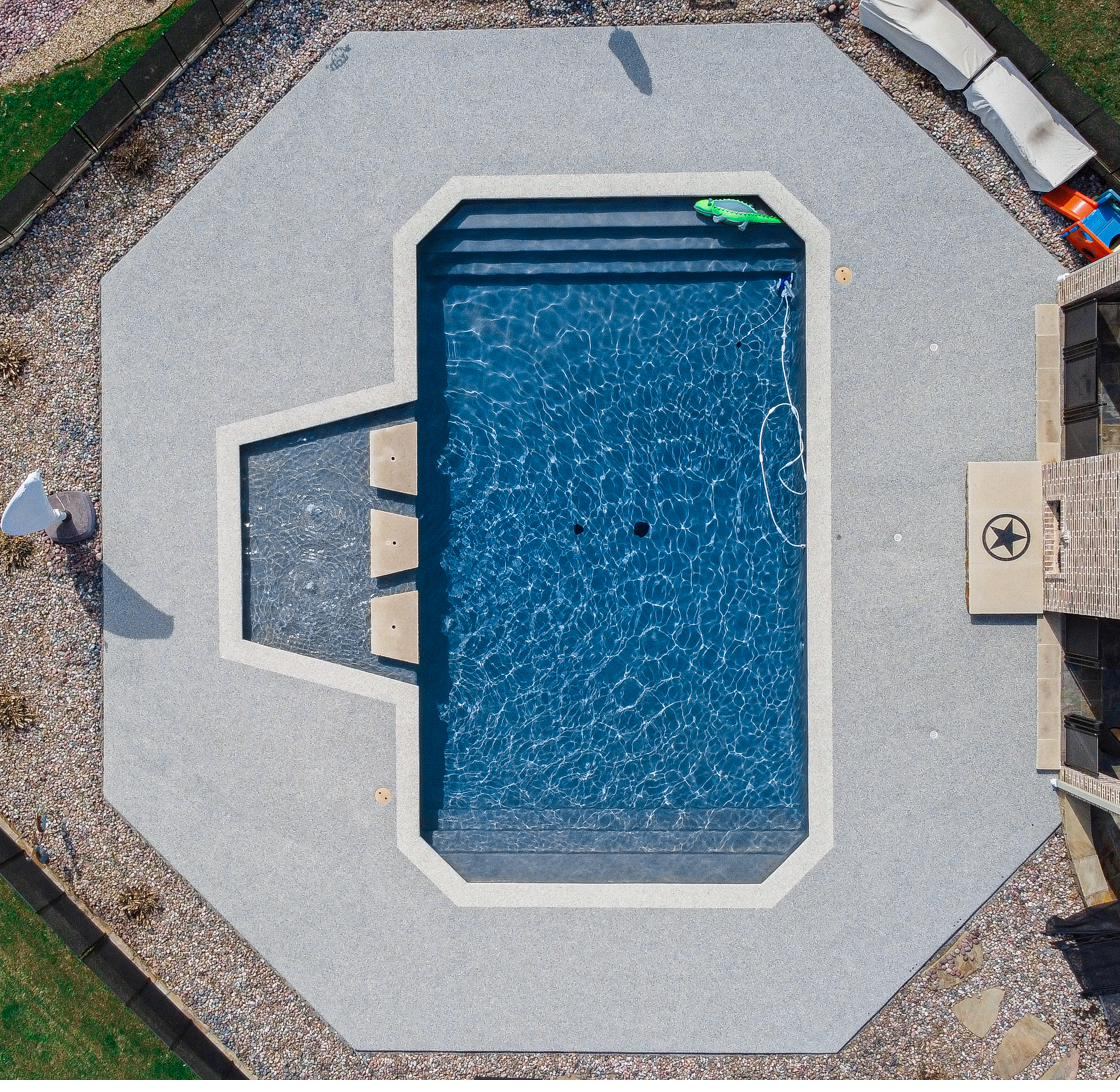 Aerial view of a freeform pool with tan poured rubber deck and artificial turf