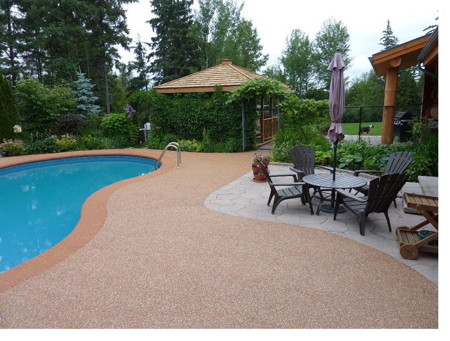 Grey speckled poured rubber deck around a kidney shaped inground pool